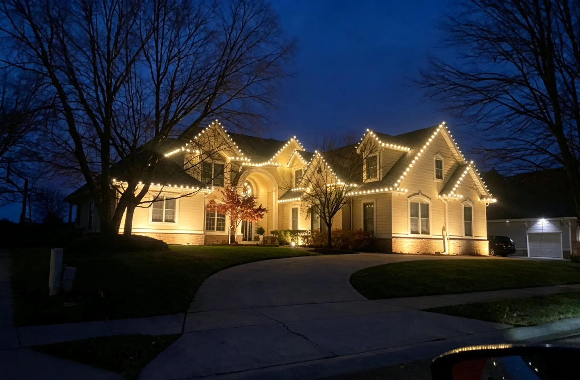 Two-story home outlined with warm white roofline holiday lights at dusk