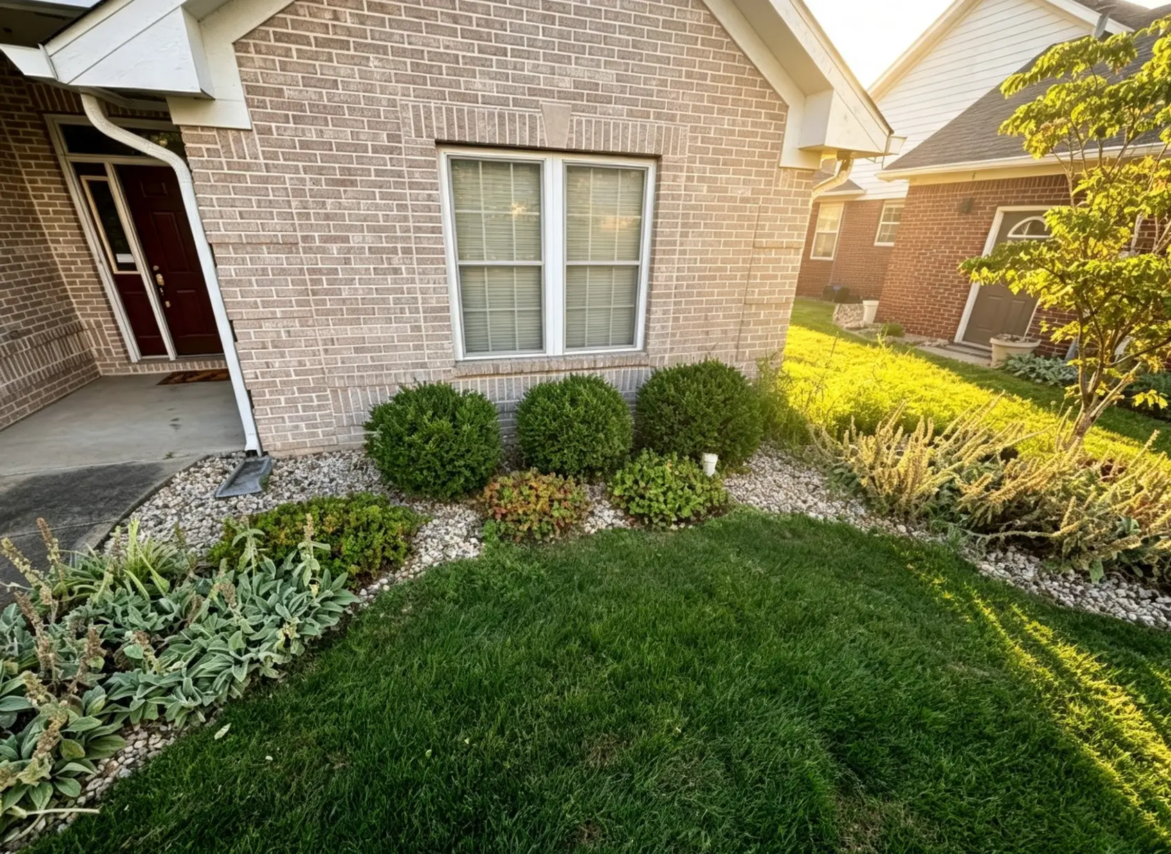 Curved decorative rock bed with shrubs and perennials installed along a brick home